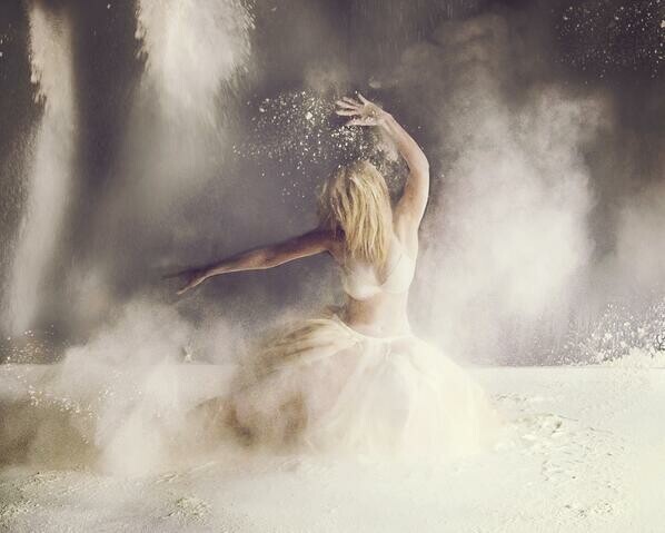 Blond dancing girl in a white tutu dances in flour, arms waving wildly, throwing puff clouds everywhere.