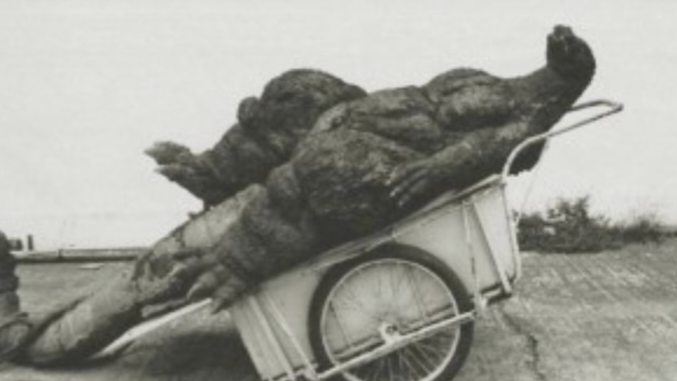 Godzilla on a trash cart getting hauled away.