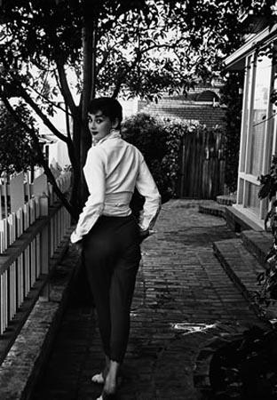 Audrey wears a white shirt and dark pants as she looks back over her shoulder.