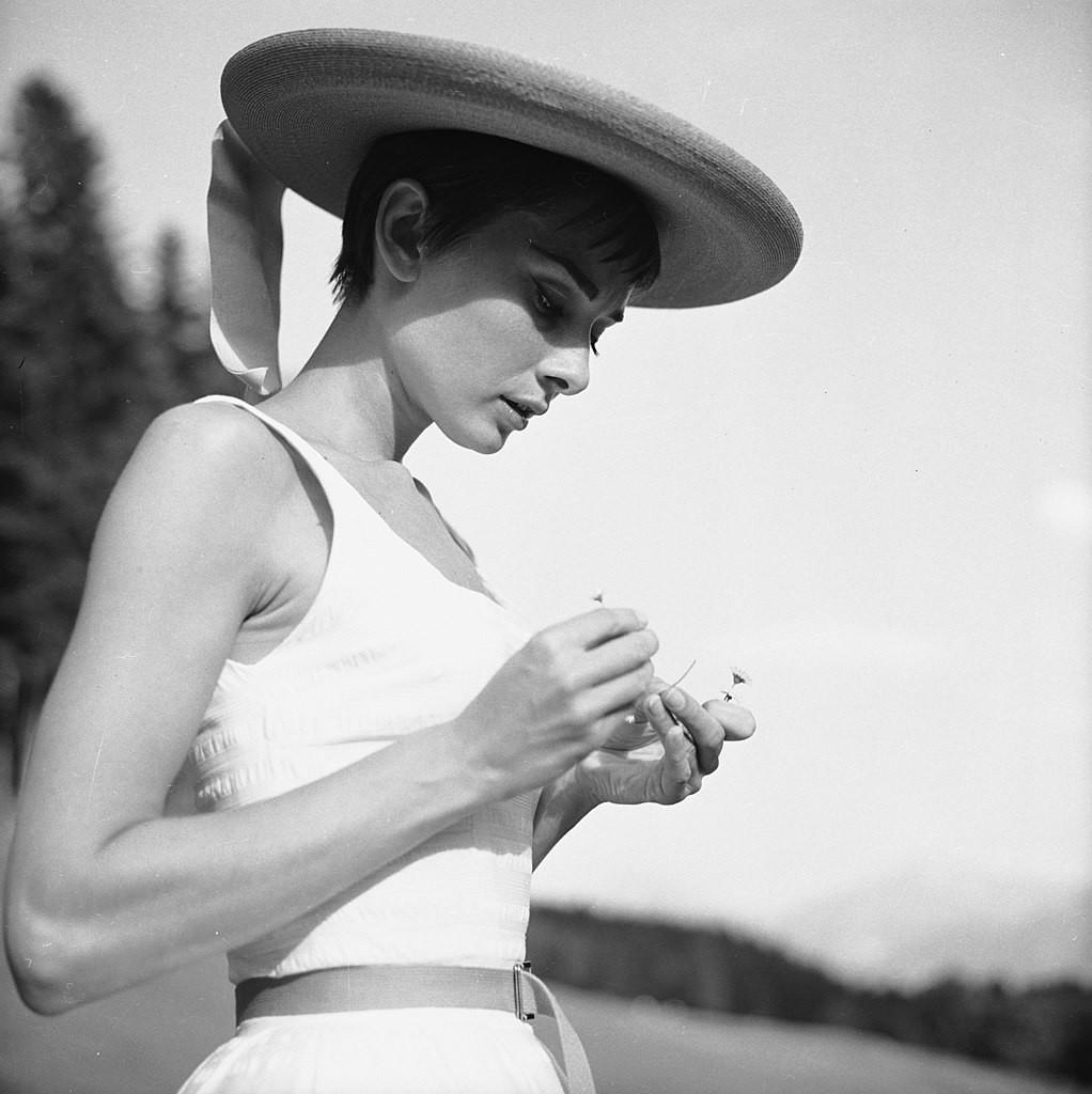 Audrey wears a white sundress and hat as she twists up a fatty in a mountain meadow.