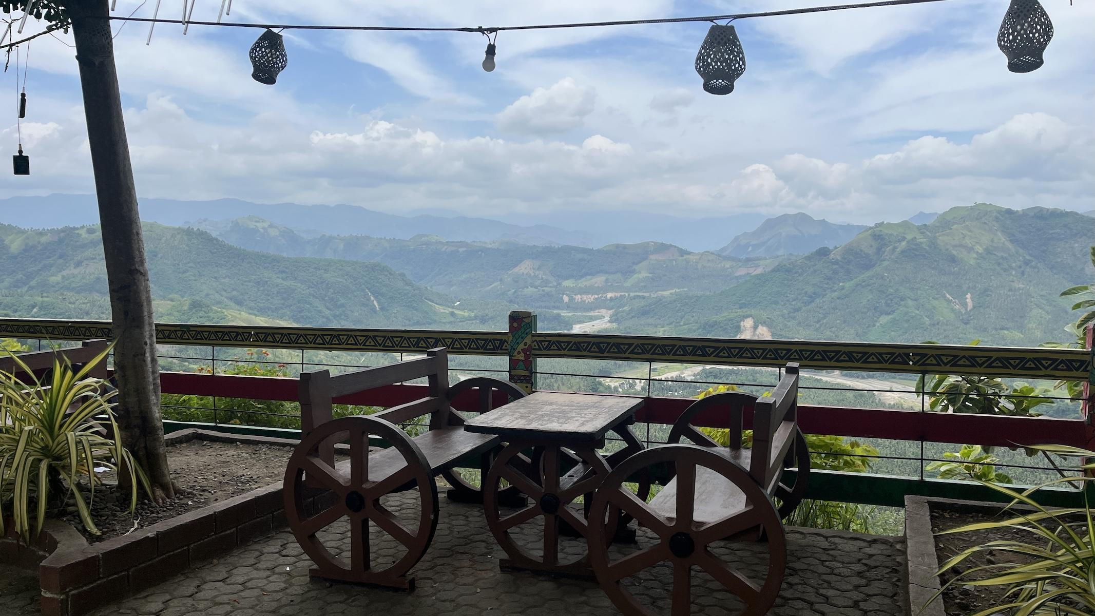A rustic table and benches at a small cafe overlooking a massive river valley surrounded by forested mountain ridges