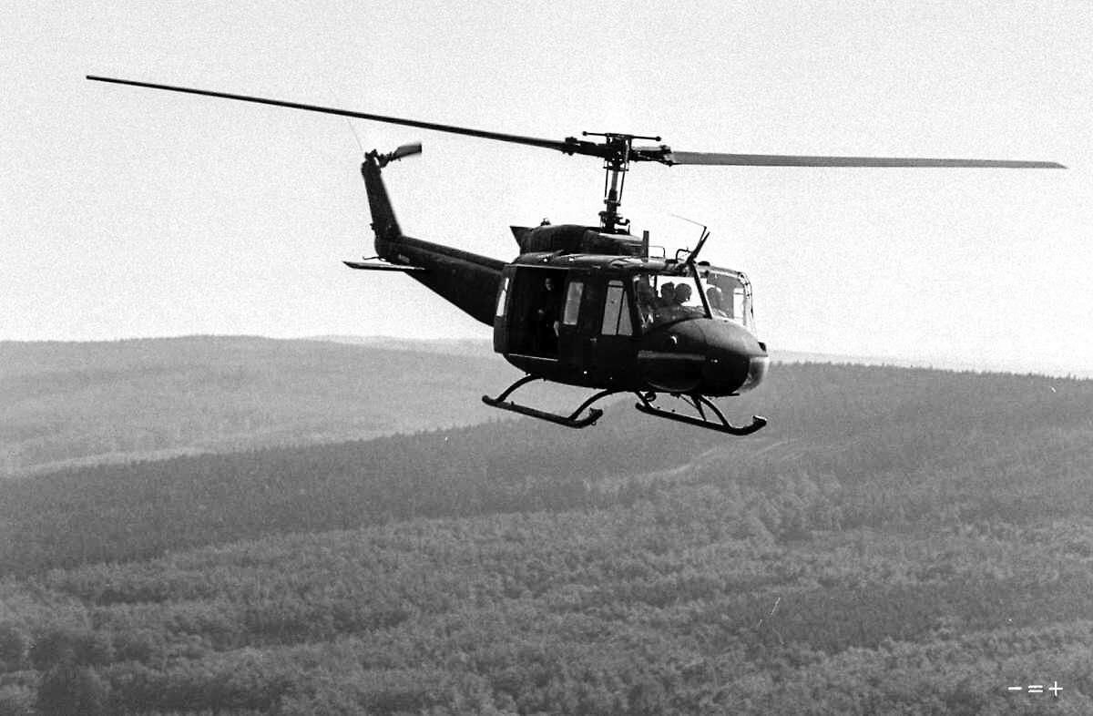 A US military helicopter Bell UH-1D is seen from its wingman in this mid-flight shot over a landscape with forest. (Foto: Michael Kaiser)